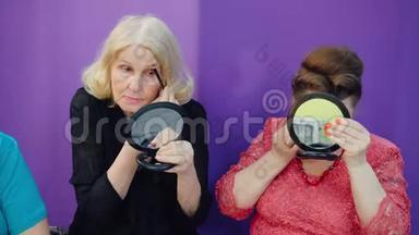 在美容学校，一位年长的妇女在脸前小镜子上<strong>化妆</strong>。 两个成熟的女人<strong>正在化妆</strong>